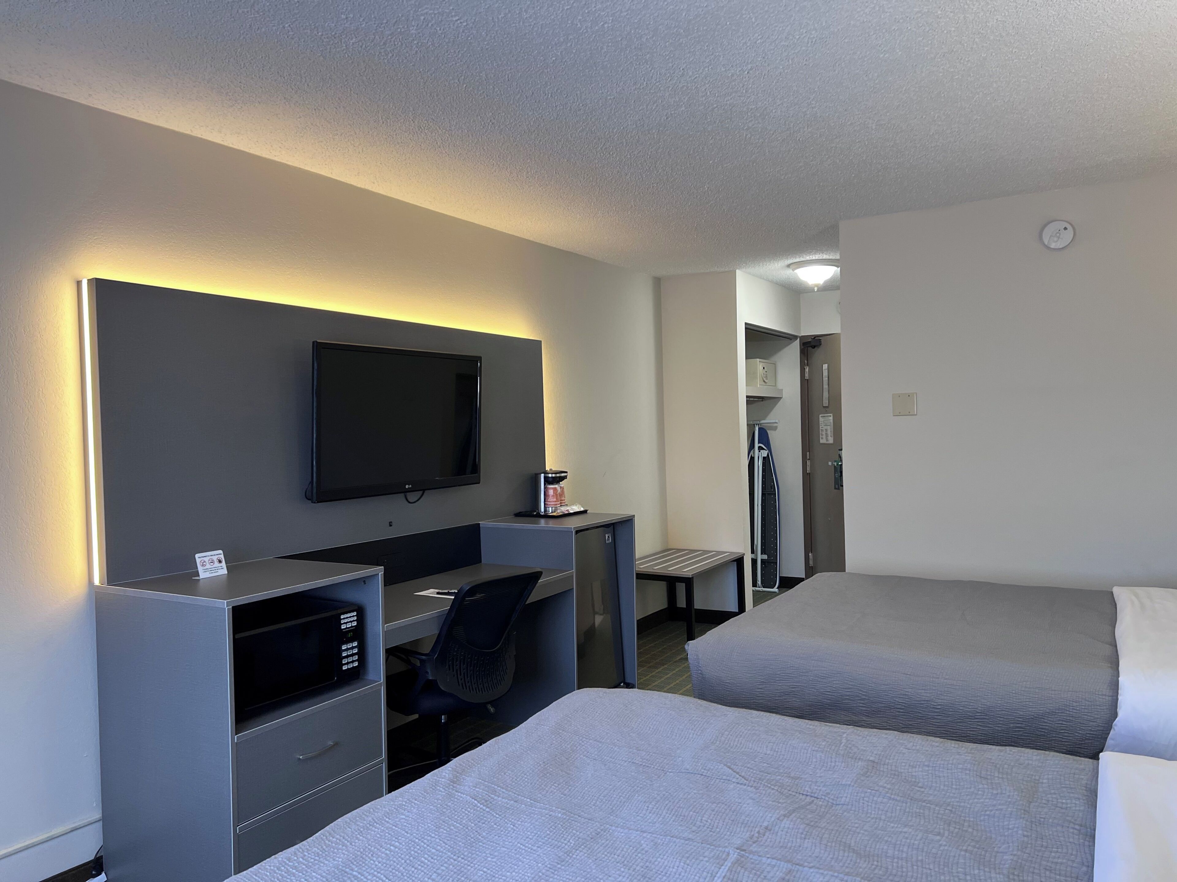 Habitación de hotel con televisión de pantalla plana, escritorio con silla, microondas y dos camas.