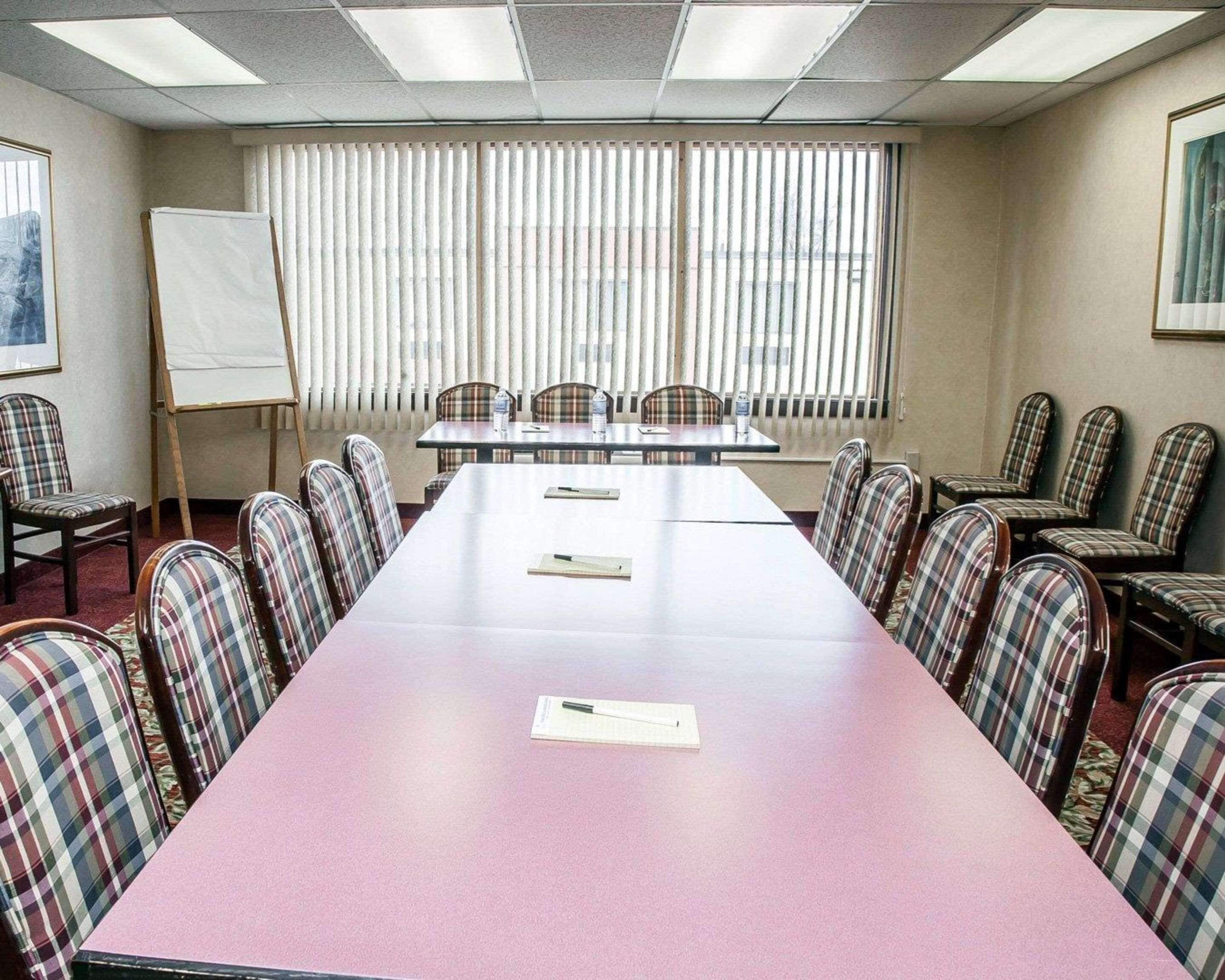 Une salle de conférence avec une longue table, des chaises à carreaux, un tableau blanc et une fenêtre avec des stores.