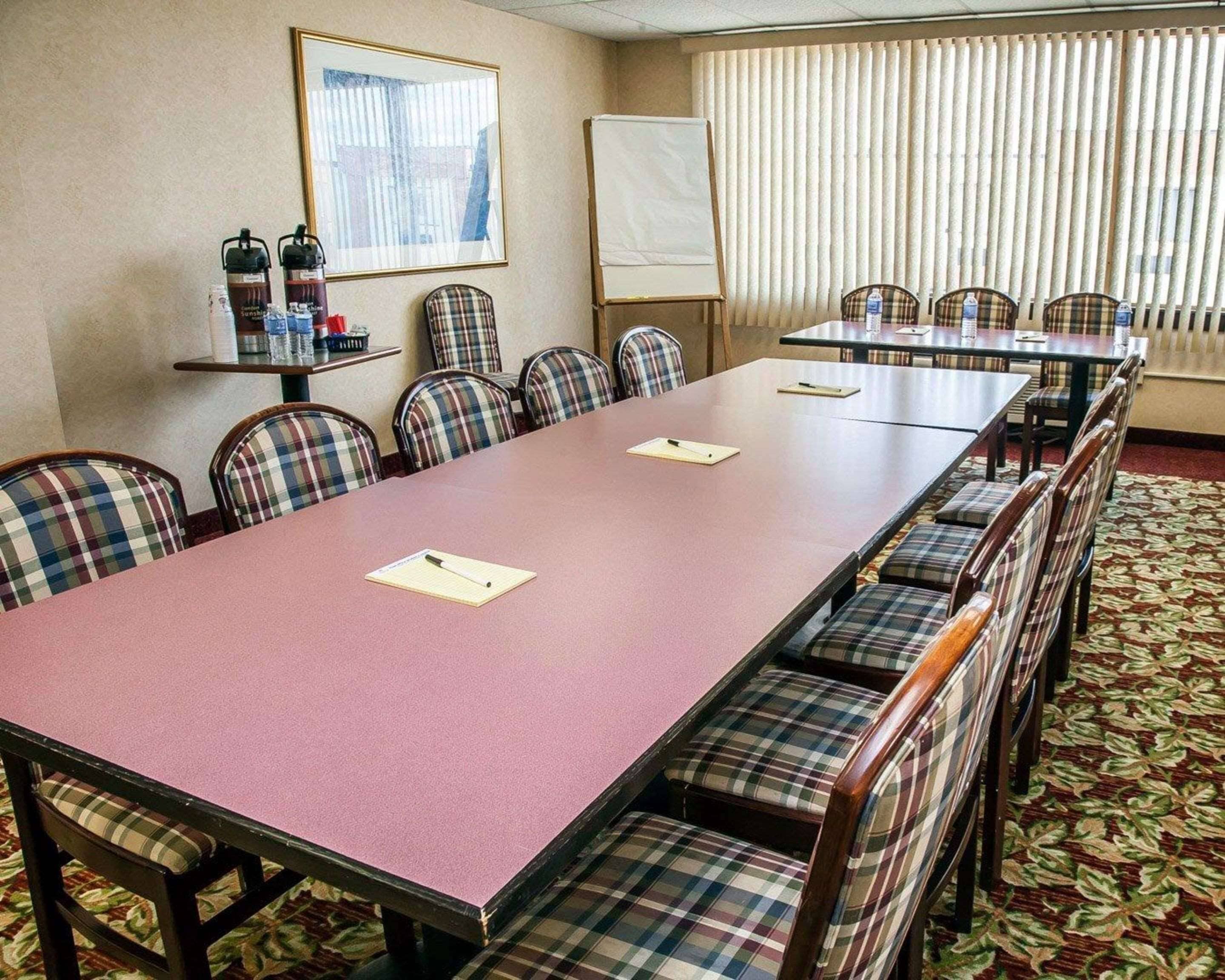 A conference room with a long table, plaid chairs, a whiteboard, and a window with blinds.