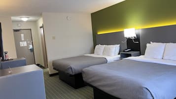 A hotel room with two beds, a desk, a coffee machine, and a door with a sign.