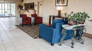 Un vestíbulo con mostrador de recepción, sillas rojas, un sofá azul y una mesa decorativa con plantas.