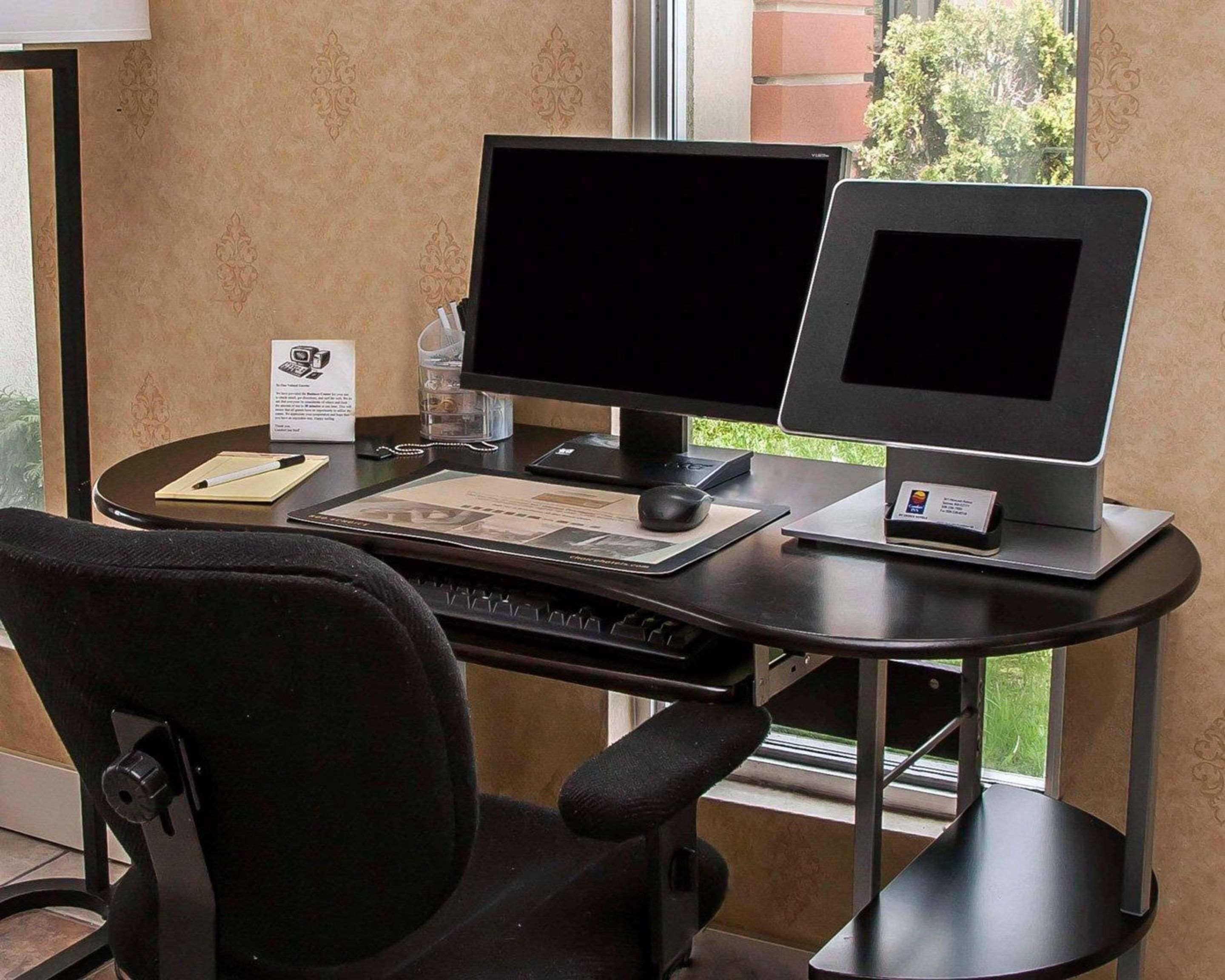 Espacio de trabajo en un hotel, con dos monitores, un teclado, un ratón y una silla.