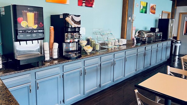 Una estación de café con una máquina de espresso Bunn, un dispensador de jugo y una exhibición de frutas frescas.