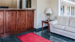 A reception area with a wooden reception desk, a red rug, a lamp, and a beige sofa. - Econo Lodge Douglassville - Pottstown (Douglassville)