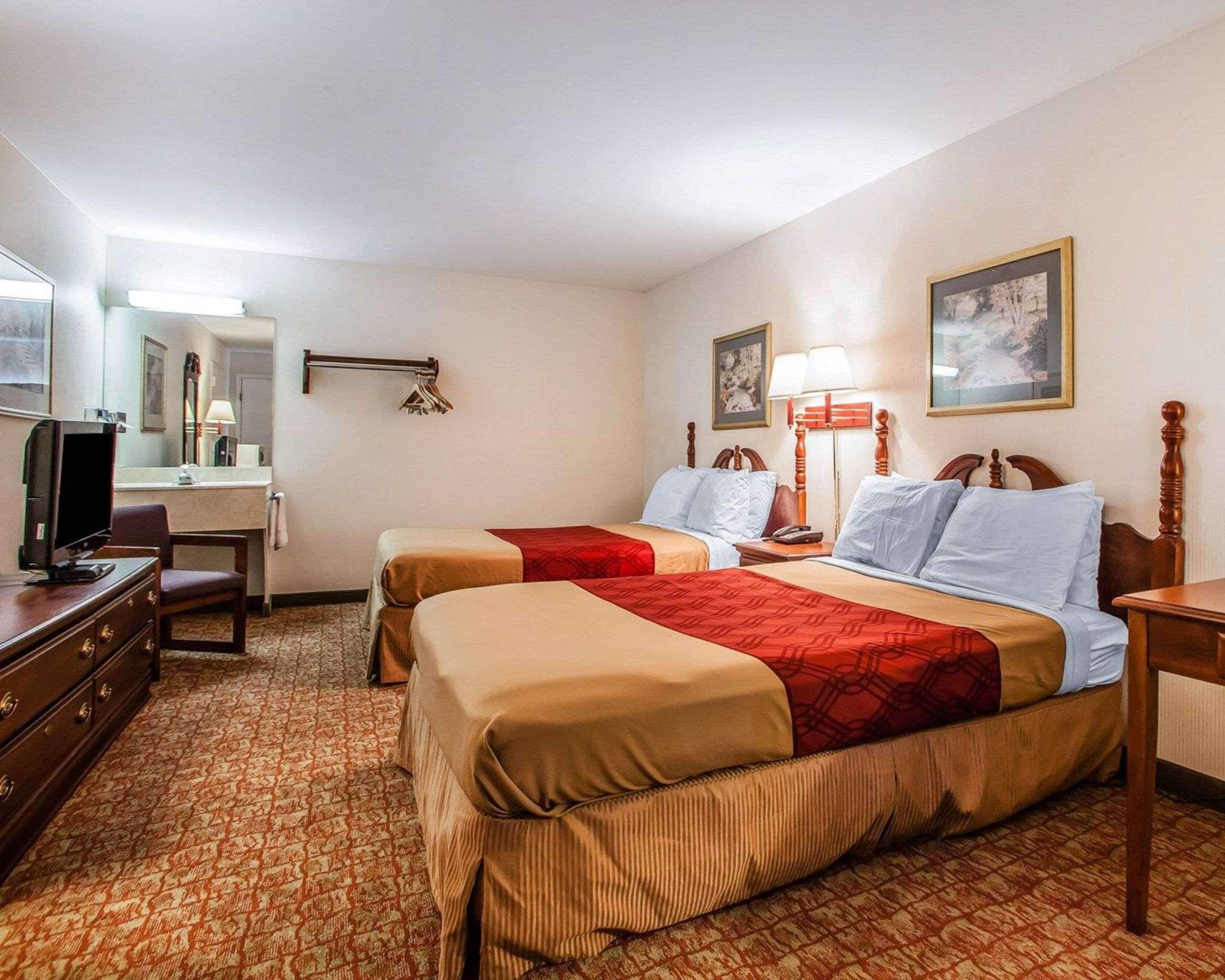 A hotel room with two beds, a desk, a television, and a mirror.