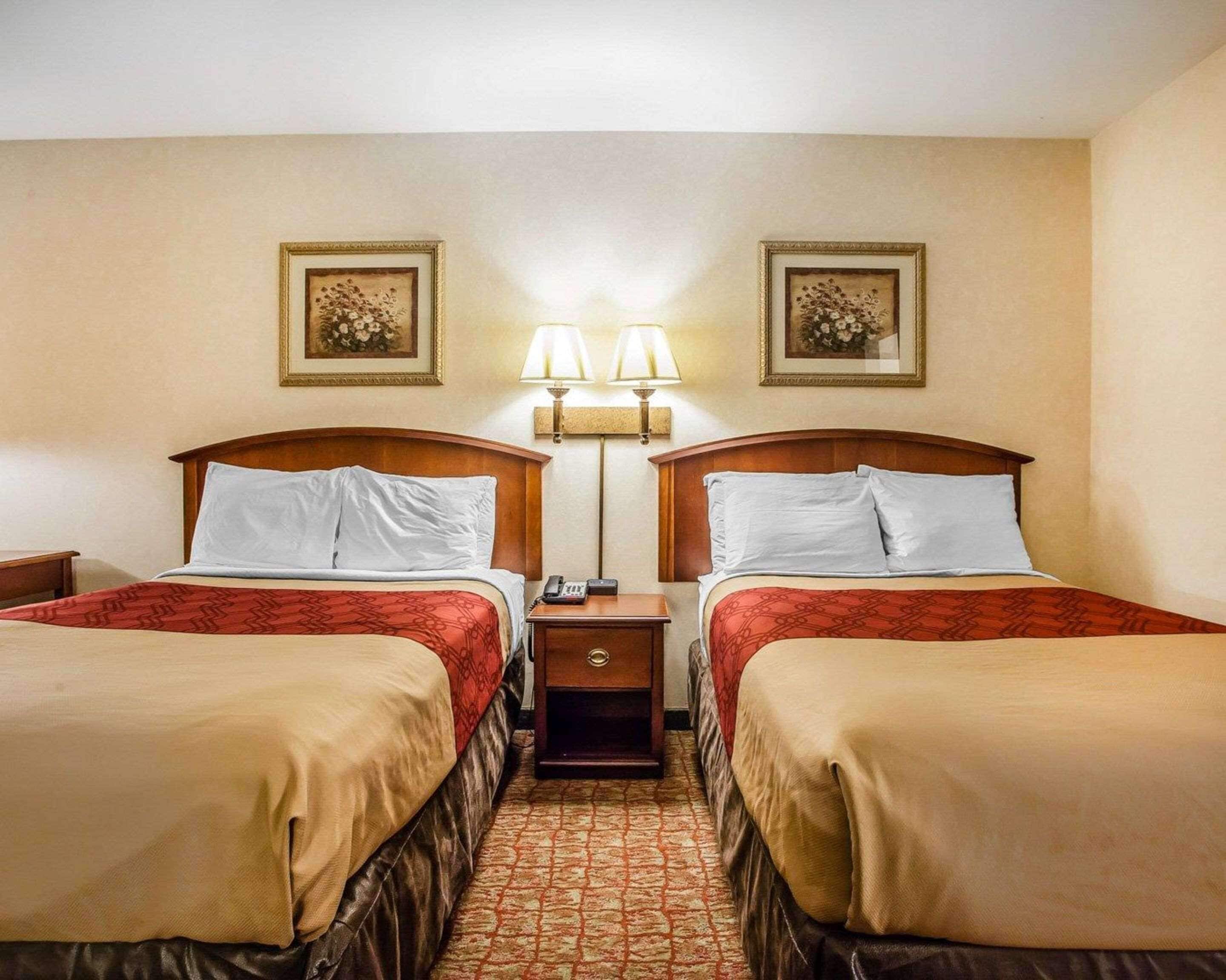 Habitación de hotel con dos camas, cada una con cabecero de madera, mesita de noche, teléfono y dos lámparas de pared.