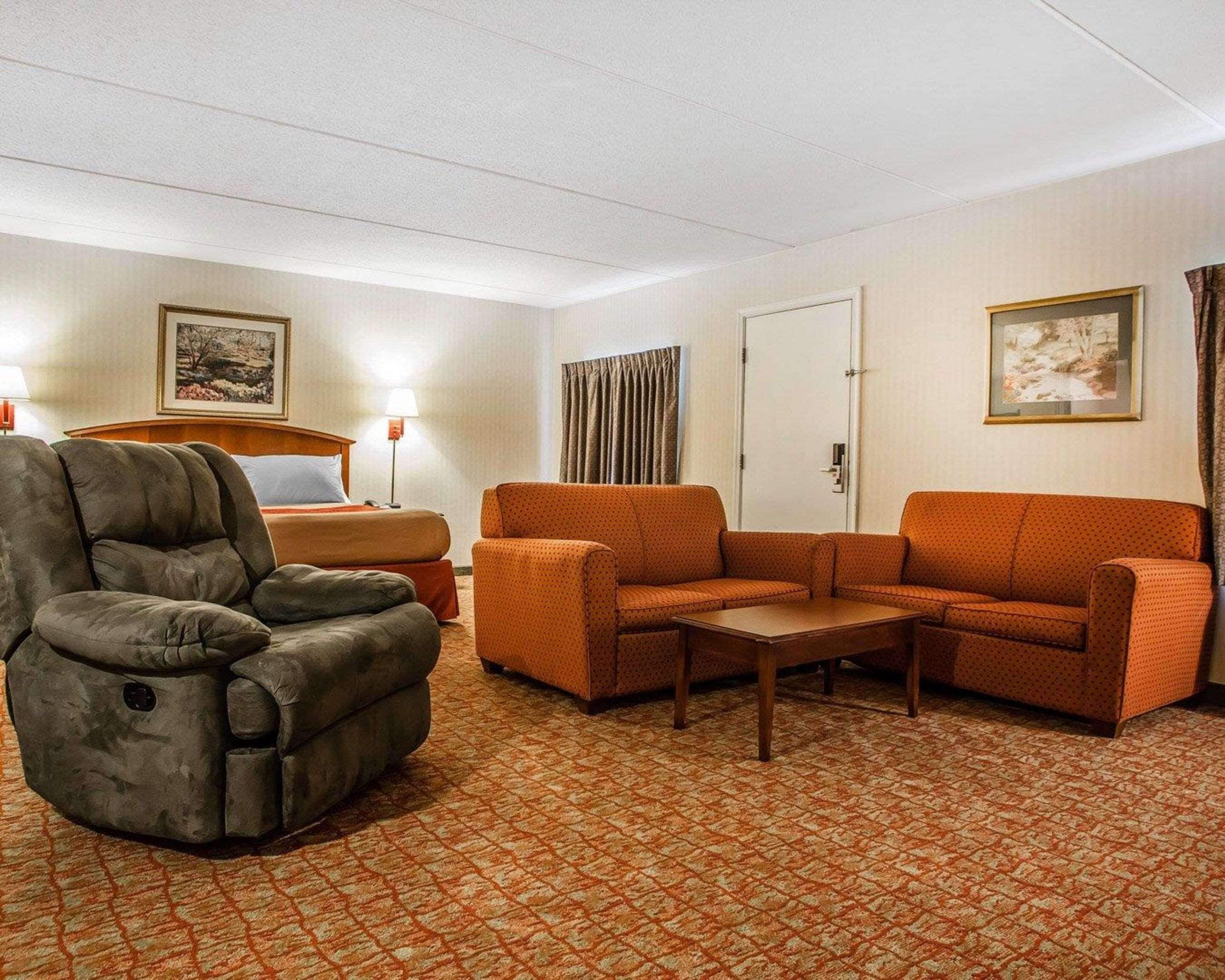 A hotel room with a bed, two armchairs, a sofa, a small table, and a carpeted floor.