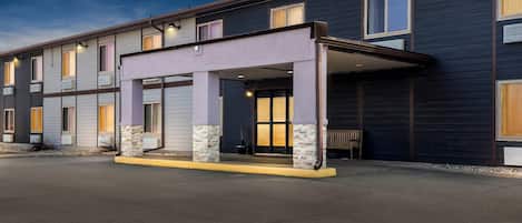 A multi-story hotel with a covered entrance, air conditioning units, and a bench outside.