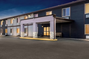 A multi-story hotel with a covered entrance, air conditioning units, and a bench outside. - Red Roof Inn & Suites Tomah (Tomah)