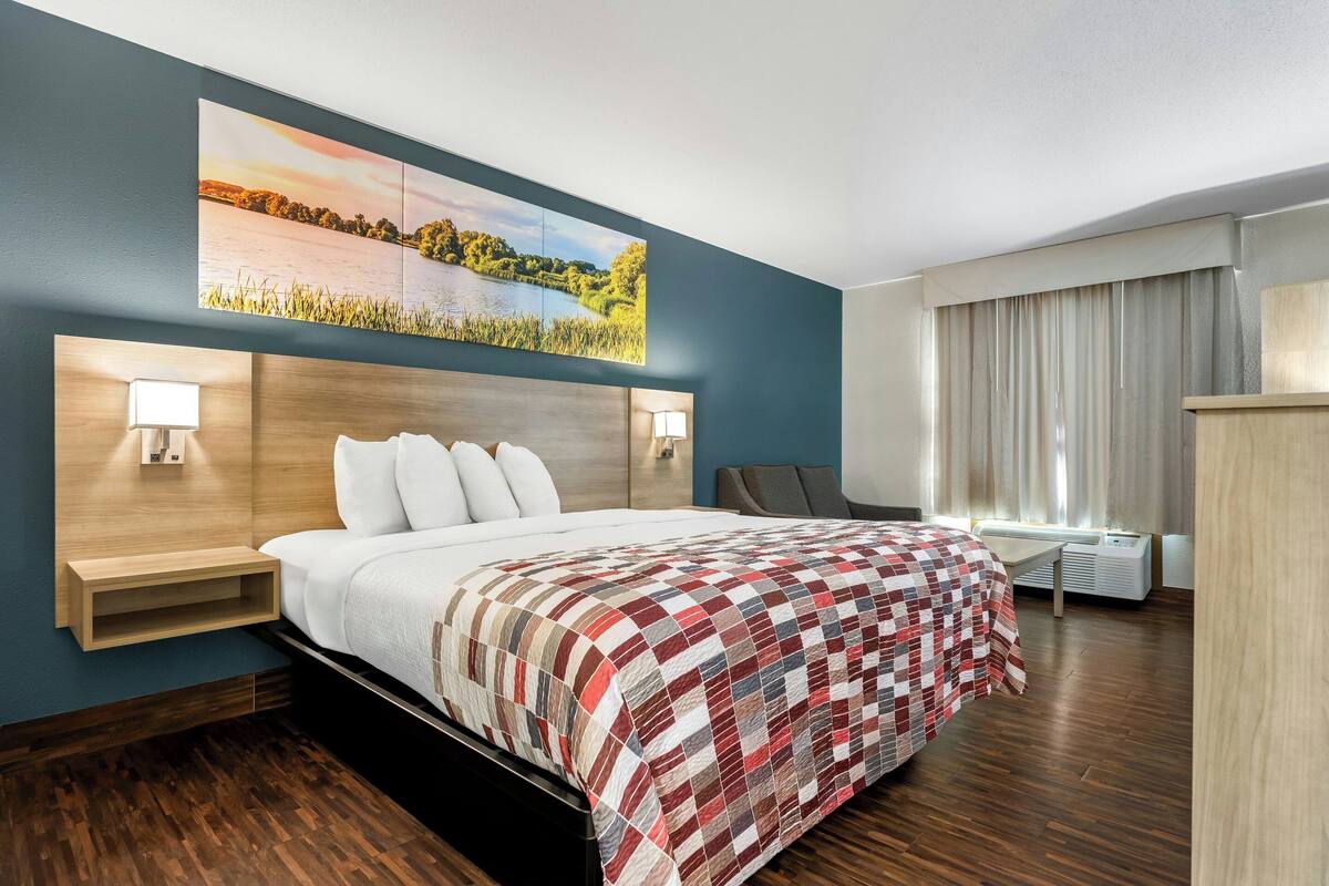 Une chambre d’hôtel avec un lit, des lampes de chevet, un tableau, un bureau et une fenêtre avec des rideaux.
