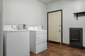 A laundry room with two front-loading washers and dryers, a door, and a small cabinet. - Red Roof Inn & Suites Tomah (Tomah)