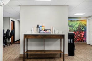 Un área de recepción con un mostrador blanco, una estación de café y un mural de un campo y tomates en la pared.