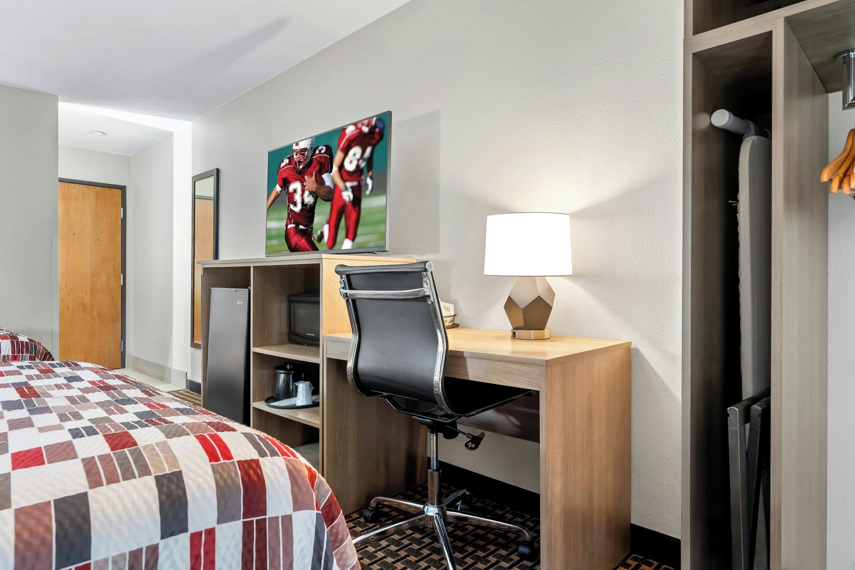 A hotel room with a bed, a desk with a chair, a television, and a wardrobe.