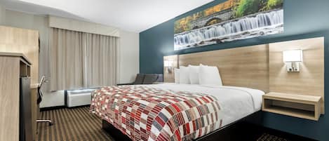 A hotel room with a bed, a painting of a waterfall, a desk, and a chair.