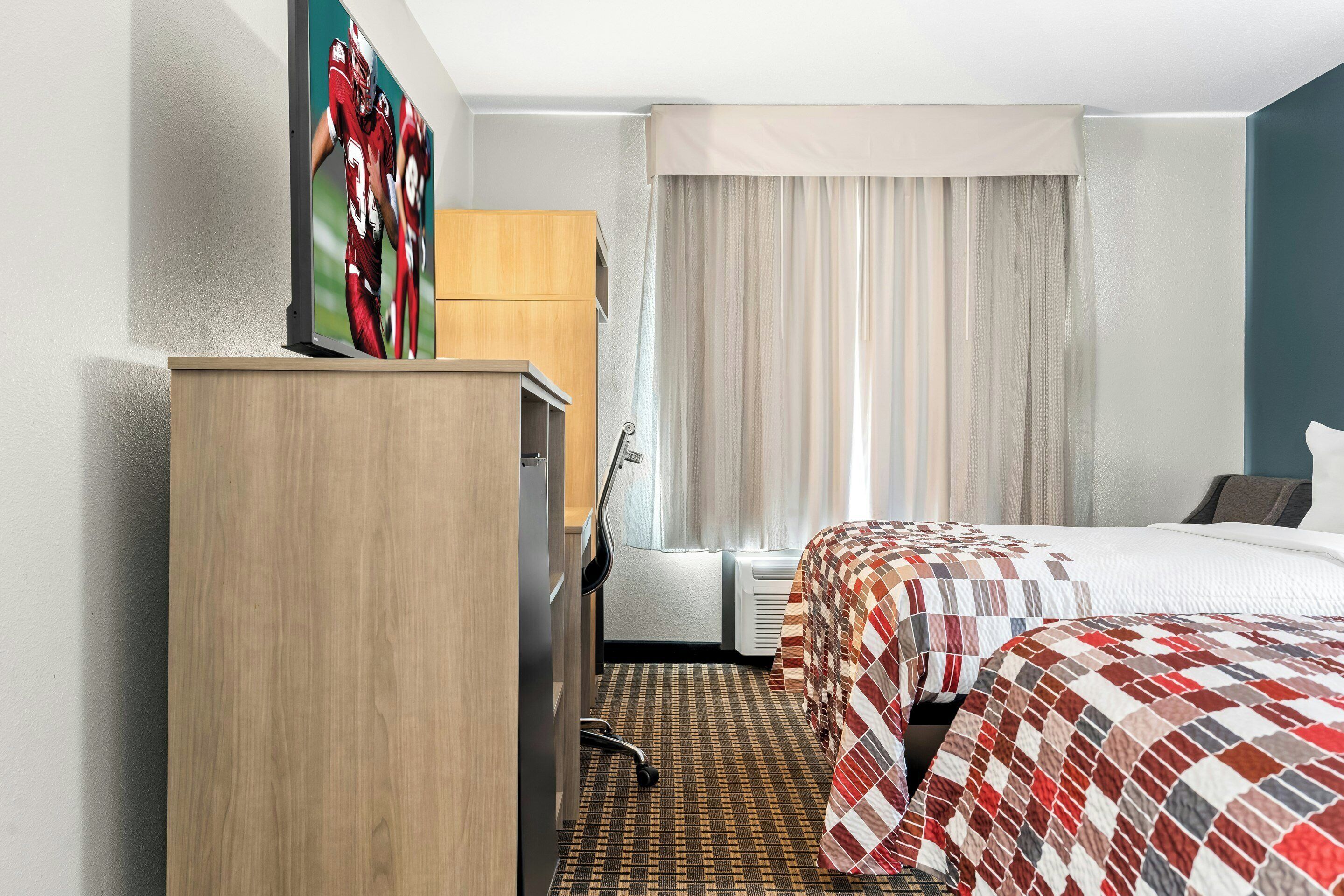 A hotel room with a bed, a desk, a chair, a wardrobe, and a window with curtains.