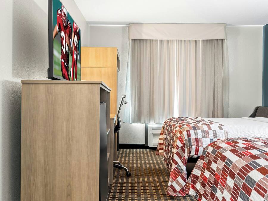 A hotel room with a bed, a desk, a chair, a wardrobe, and a window with curtains.