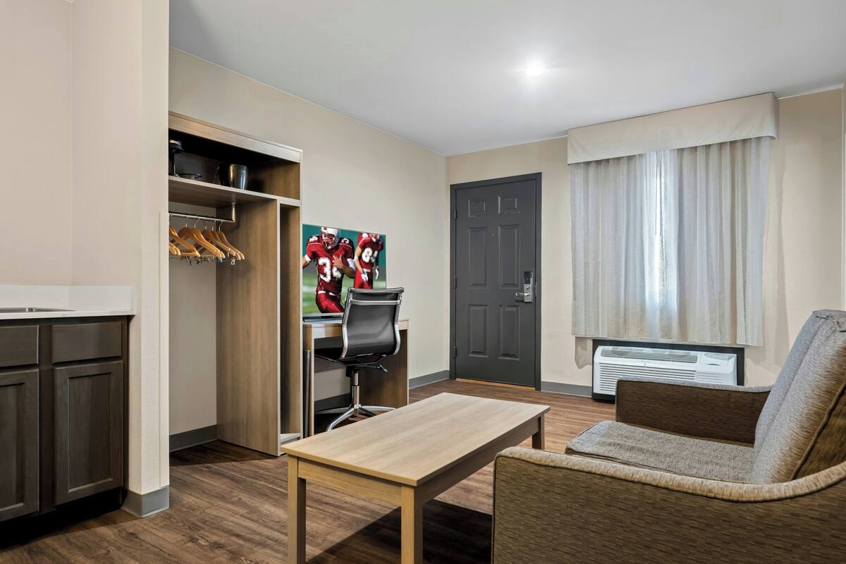 Une chambre d’hôtel équipée d’une kitchenette, d’une table à manger, d’un canapé, d’une porte et d’une fenêtre avec des rideaux.