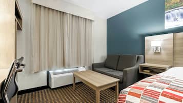 Een hotelkamer met een bed, een klein tafeltje, een sofa, een raam met gordijnen, een wandlamp en een radiator.