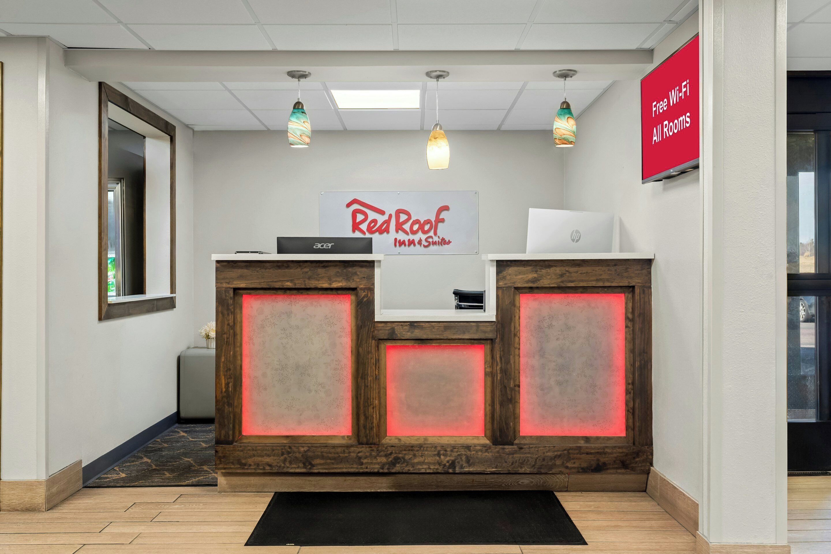 Una recepción con un cartel de Red Roof Inn & Suites, una laptop Acer y un letrero que indica Wi-Fi gratuito en todas las habitaciones.