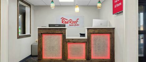 A reception desk with a Red Roof Inn & Suites sign, an Acer laptop, and a sign indicating free Wi-Fi in all rooms.