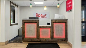 Una recepción con un cartel de Red Roof Inn & Suites, una laptop Acer y un letrero que indica Wi-Fi gratuito en todas las habitaciones.