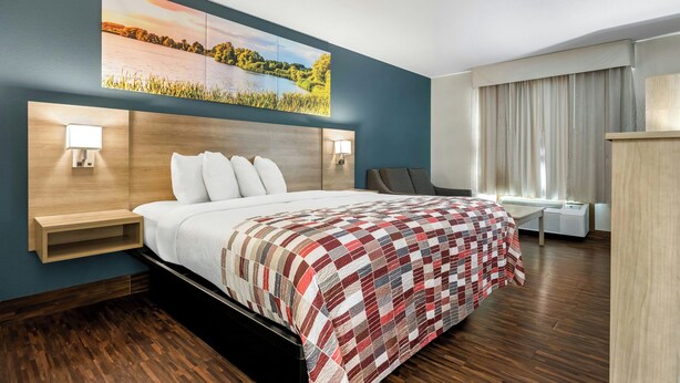 A hotel room with a bed, bedside lamps, a painting, a desk, and a window with curtains. - Red Roof Inn & Suites Tomah (Tomah)