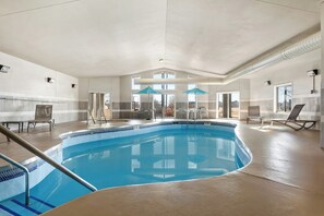 Una piscina interior con vista despejada, sillas de descanso y un techo con una lámpara central.