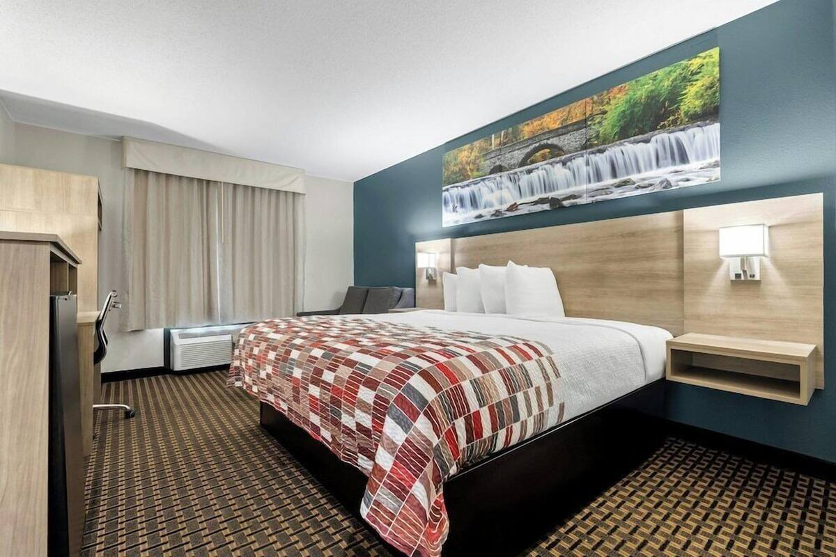 Une chambre d’hôtel avec un grand lit, une tête de lit ornée d’un tableau, un bureau avec une chaise et une lampe fixée au mur.