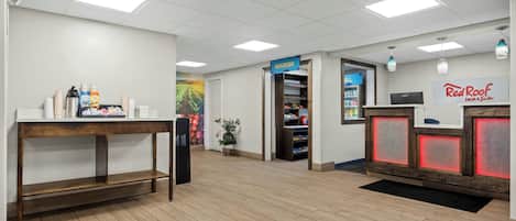 Un área de recepción con un escritorio de madera, un refrigerador, una estación de café y el letrero de Red Roof Inn.
