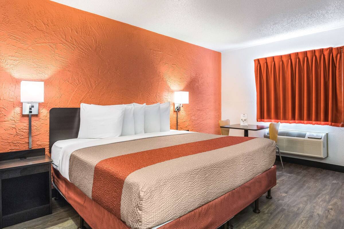 A hotel room with a bed, bedside lamps, a desk, and a window with curtains.