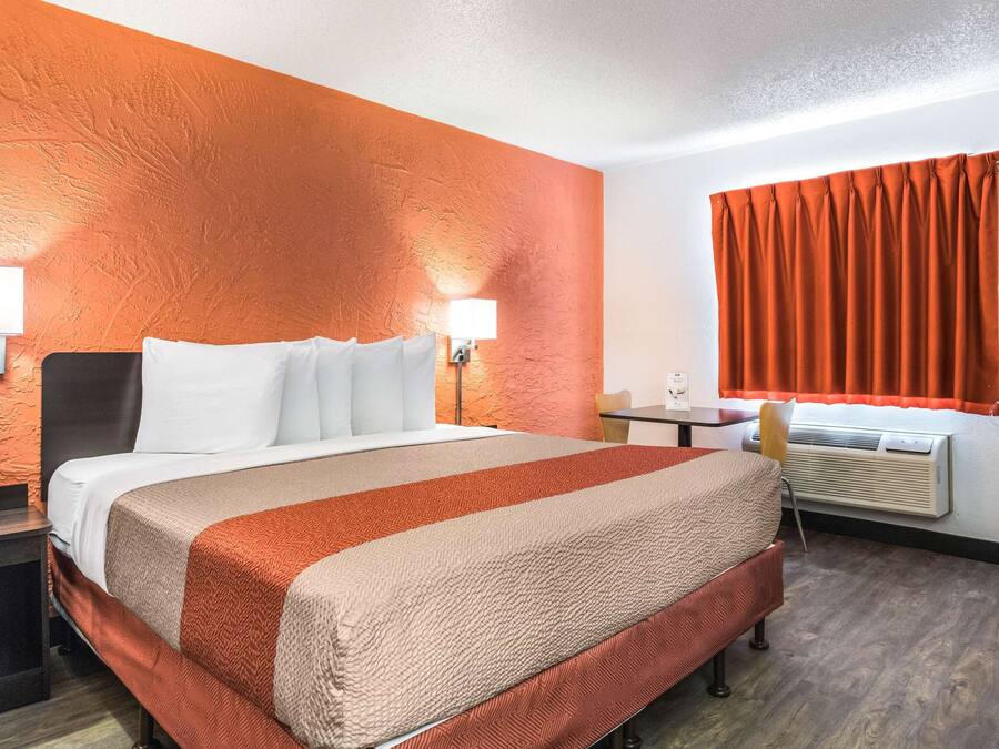 A hotel room with a bed, bedside lamps, a desk, and a window with curtains.