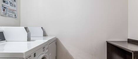 A laundry area with a front-loading washing machine and dryer, a small shelf, and a wall-mounted instruction poster.