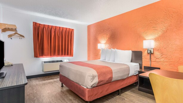 A hotel room with a bed, bedside tables, a desk, a chair, a wardrobe, and a window with curtains. - Motel 6 Elk Grove Village, IL (Elk Grove Village)