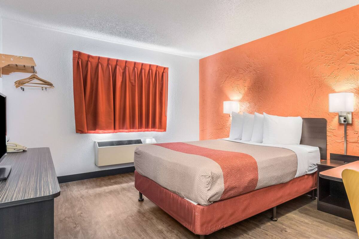 A hotel room with a bed, bedside tables, a desk, a chair, a wardrobe, and a window with curtains.