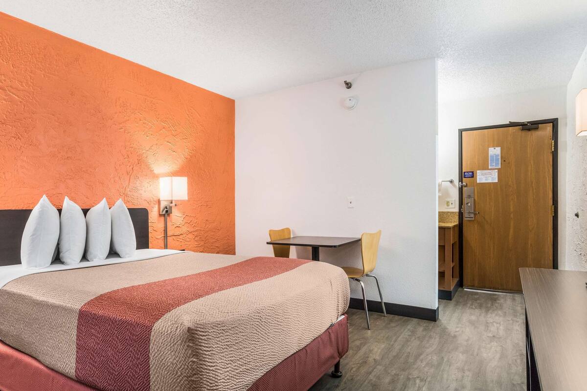 A hotel room with a bed, a desk, a chair, and a door.