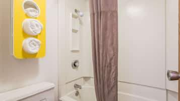 A bathroom with a yellow towel rack holding three towels, a shower with a brown curtain, and a white door.