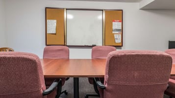 A conference room with a wooden table, four pink patterned chairs, and two bulletin boards with safety and security notices.