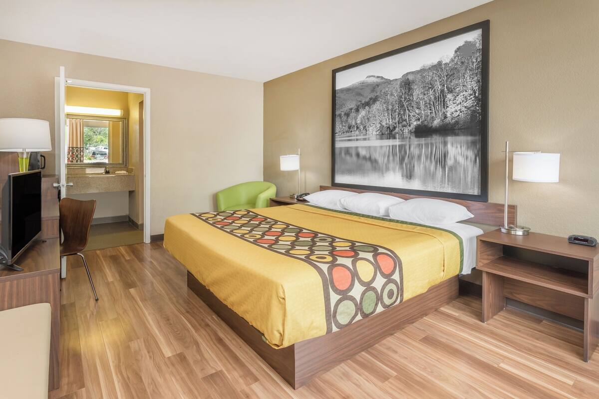 A hotel room with a bed, a desk with a computer, a chair, and a large window.