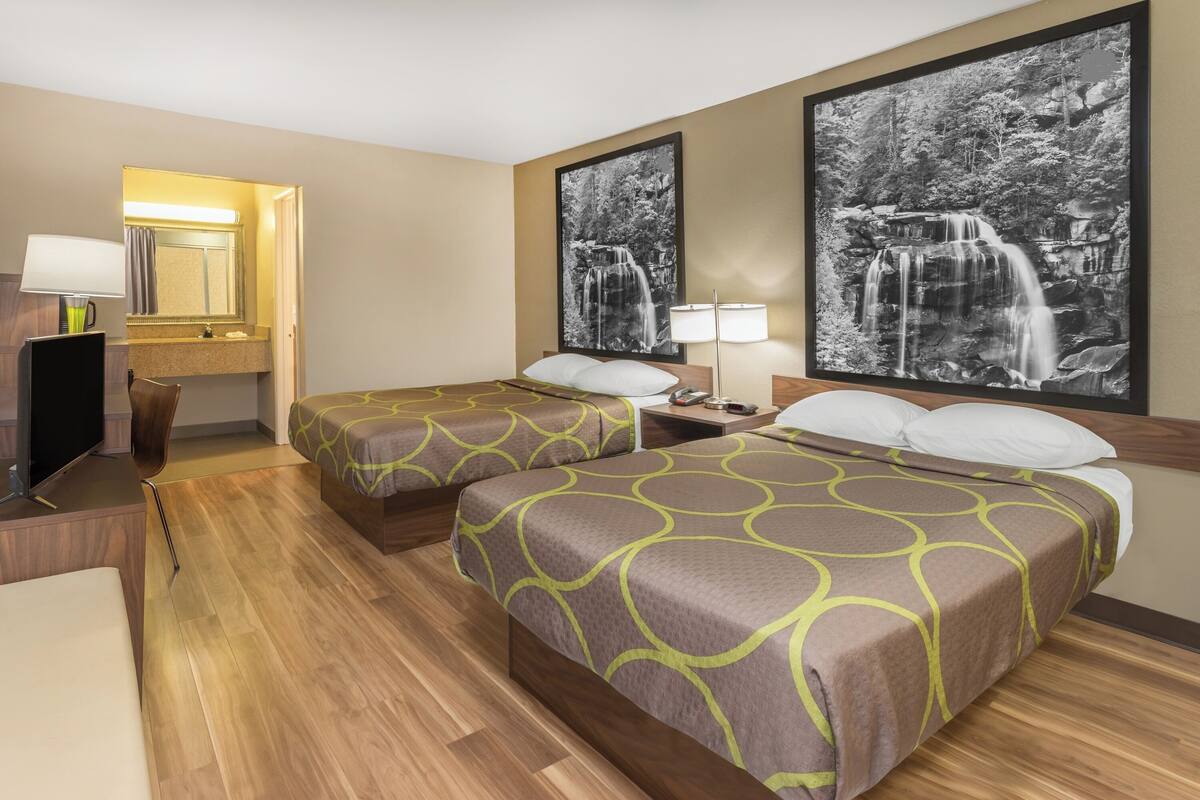 A hotel room with two beds, a TV, a desk, and a bathroom mirror.