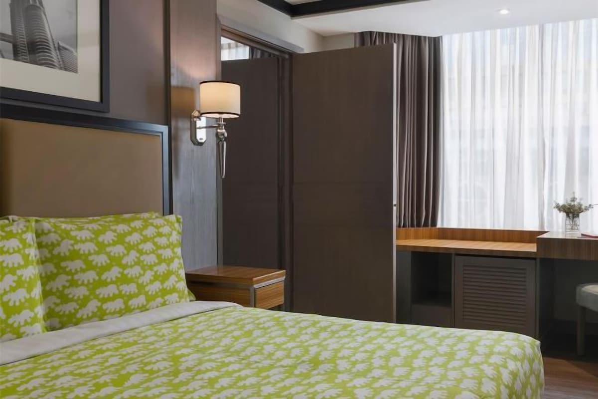 A hotel room with a bed, a desk, a lamp, and a window with curtains.