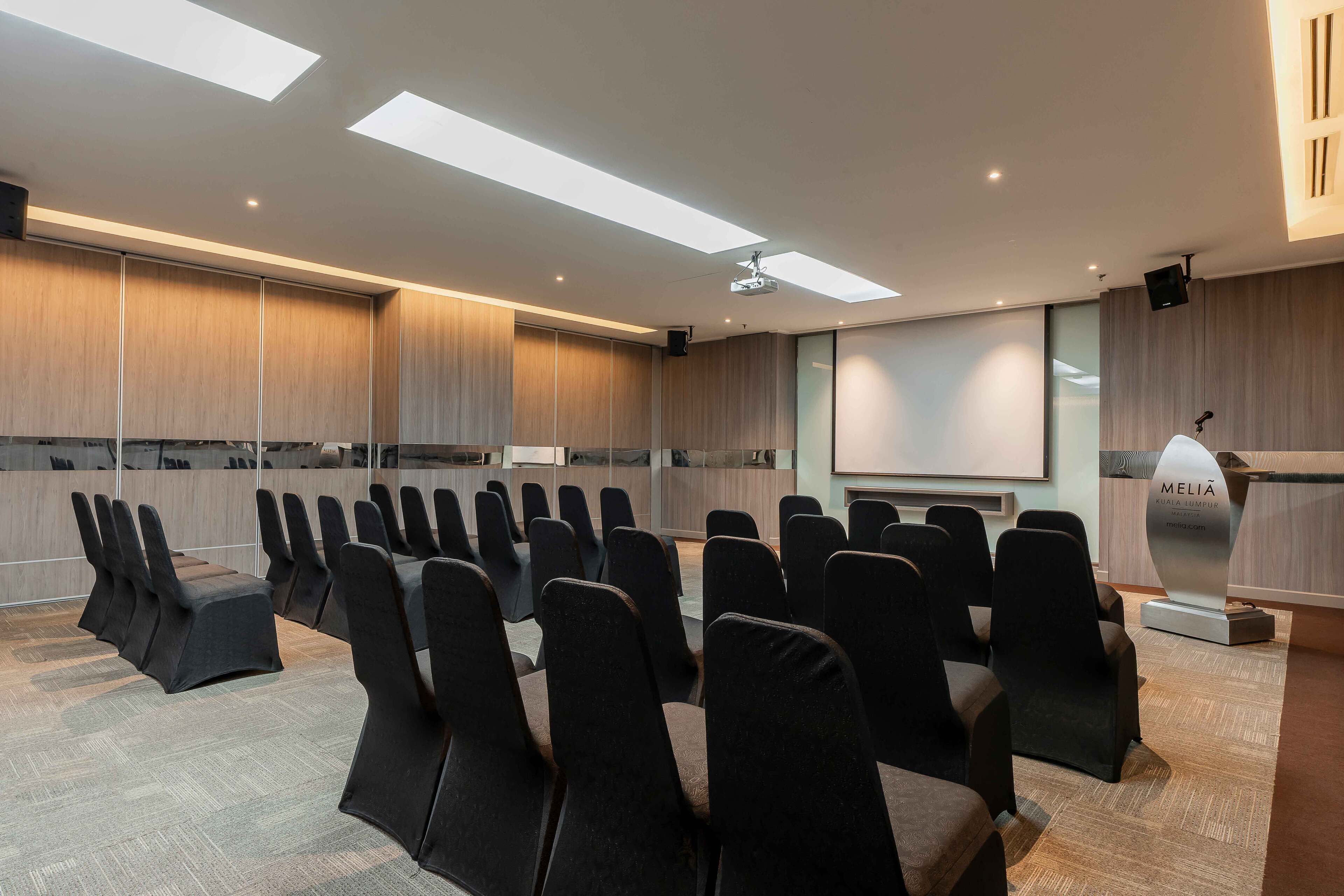 A conference room with rows of chairs, a projector screen, and a reception desk.