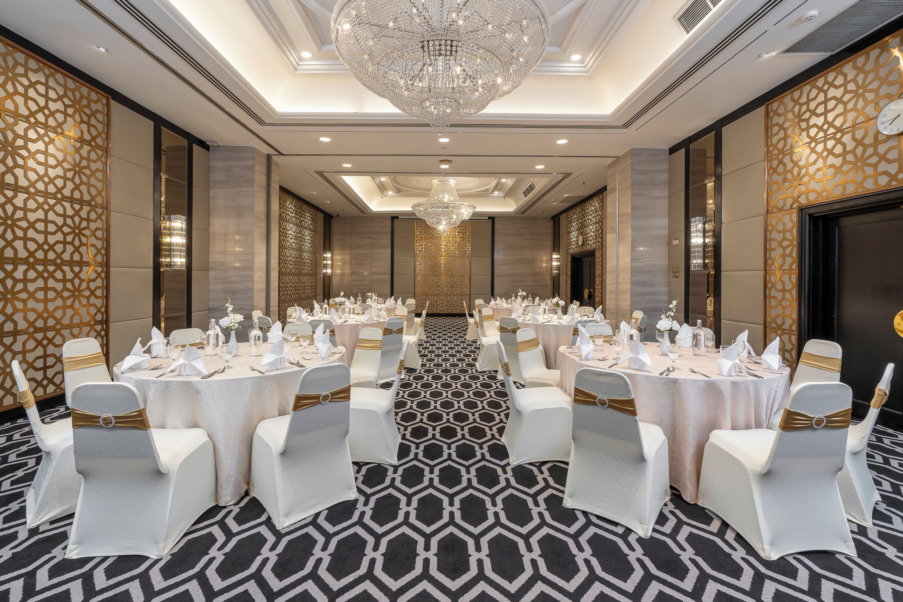 A banquet hall with round tables, white chairs, and a large chandelier.