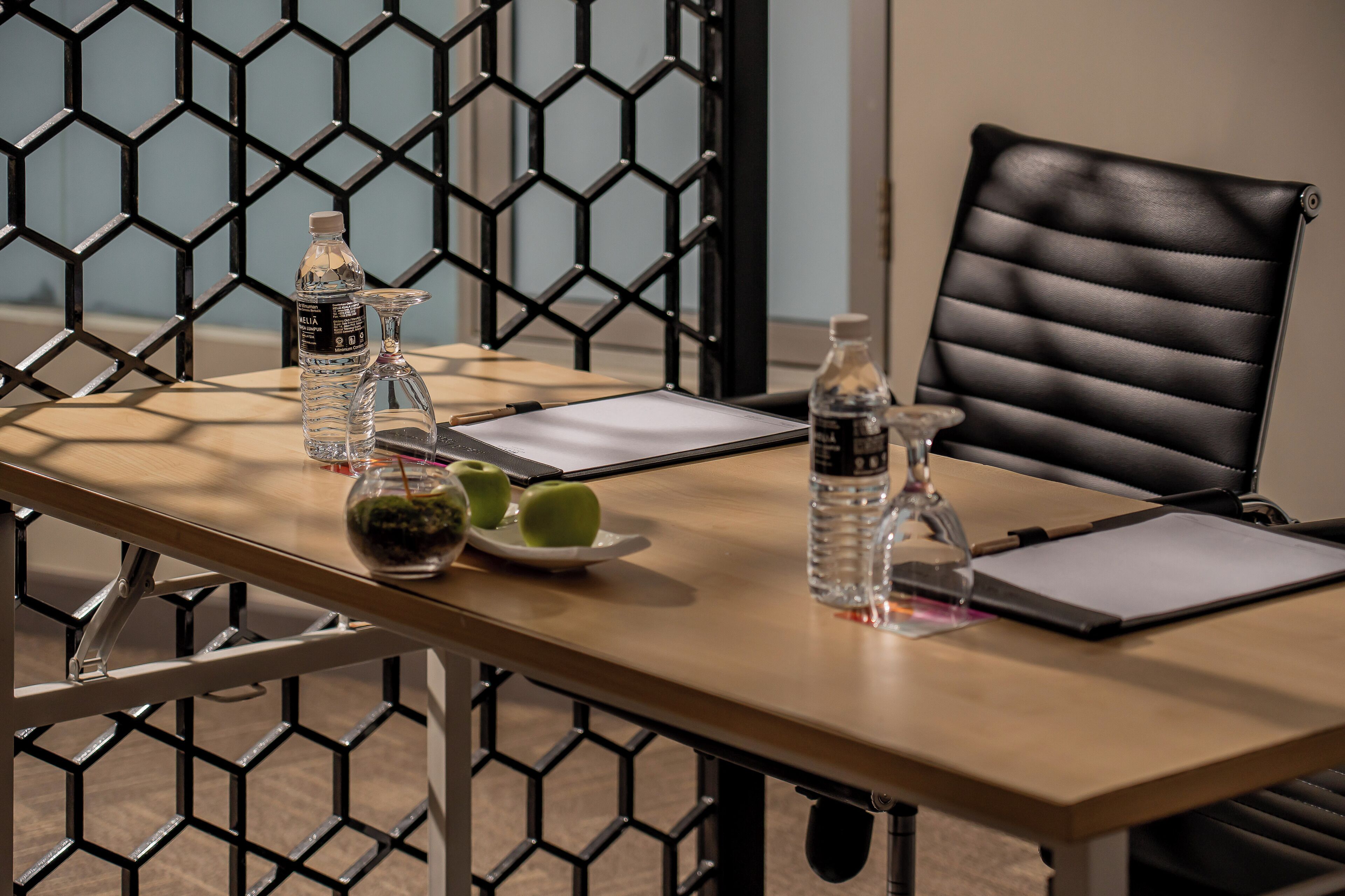 A conference table with water bottles, a glass, a plate with apples, and a black leather chair.