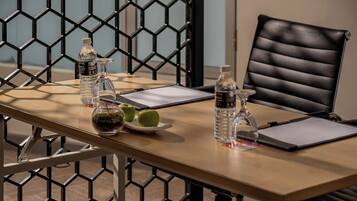 A conference table with water bottles, a glass, a plate with apples, and a black leather chair.
