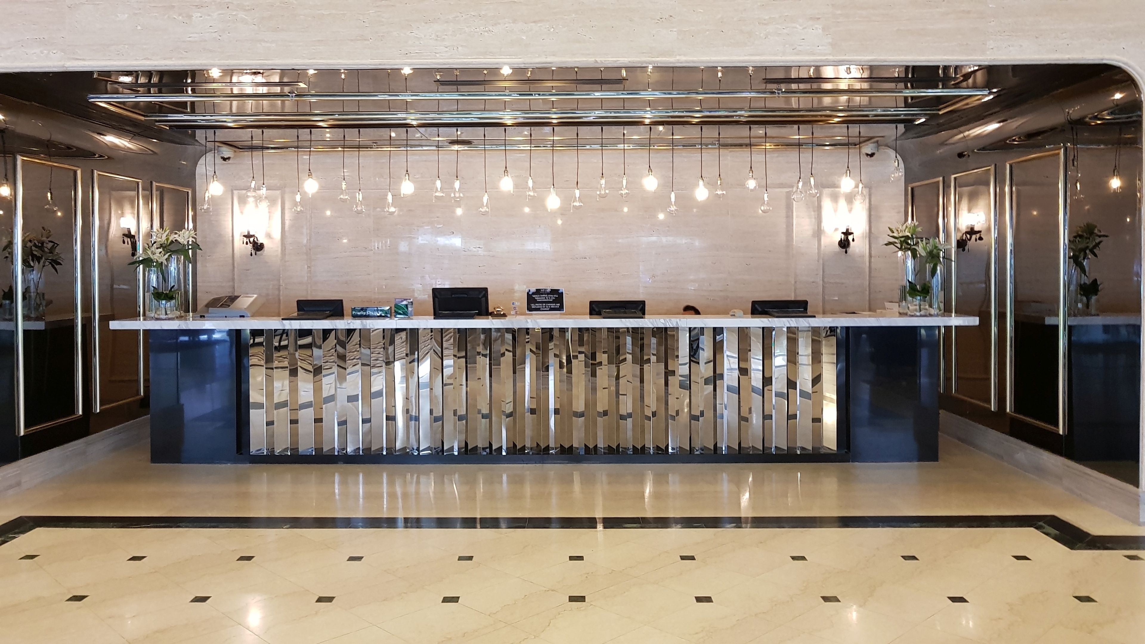 A reception desk with a modern design, featuring a glass partition, a metal frame, and a hanging light fixture.