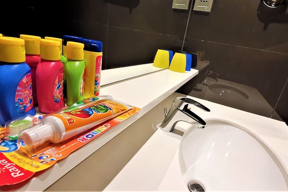 A bathroom with a white sink, a mirror, and various toiletries including bottles and a tube of toothpaste.