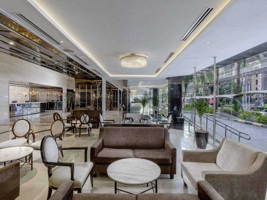 A modern lobby with seating areas, a chandelier, and a view of the street through large windows.