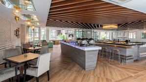 A modern restaurant with a central island, high ceilings with wooden beams, and a brick wall. - Melia Kuala Lumpur (Kuala Lumpur)