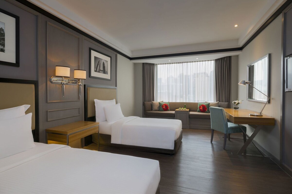 Habitación de hotel con dos camas, un escritorio y una ventana con cortinas.