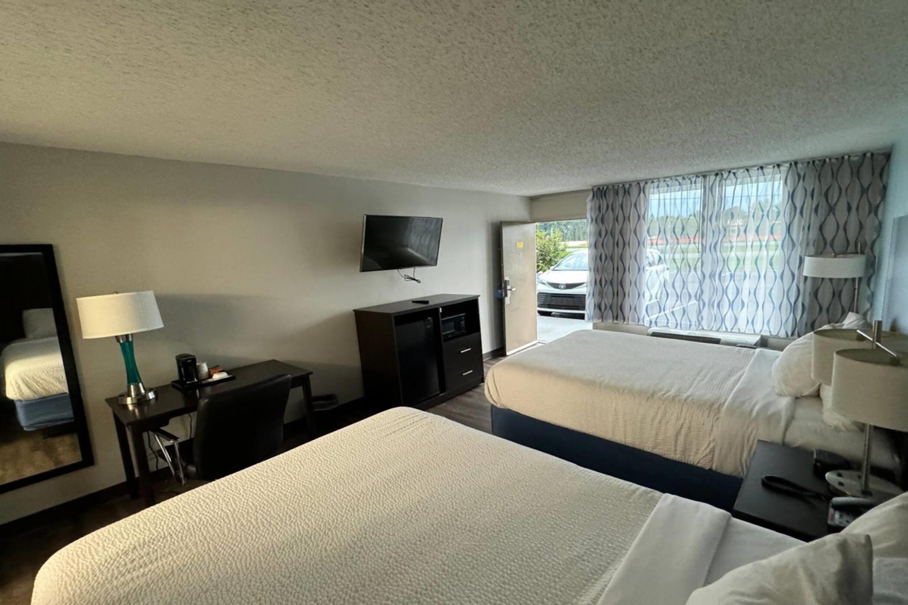 A hotel room with two beds, a desk, a TV, and a window with curtains.